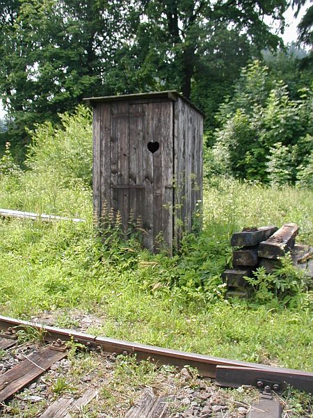Vyšší neudržovaná vegetace kolem drobné stavby
